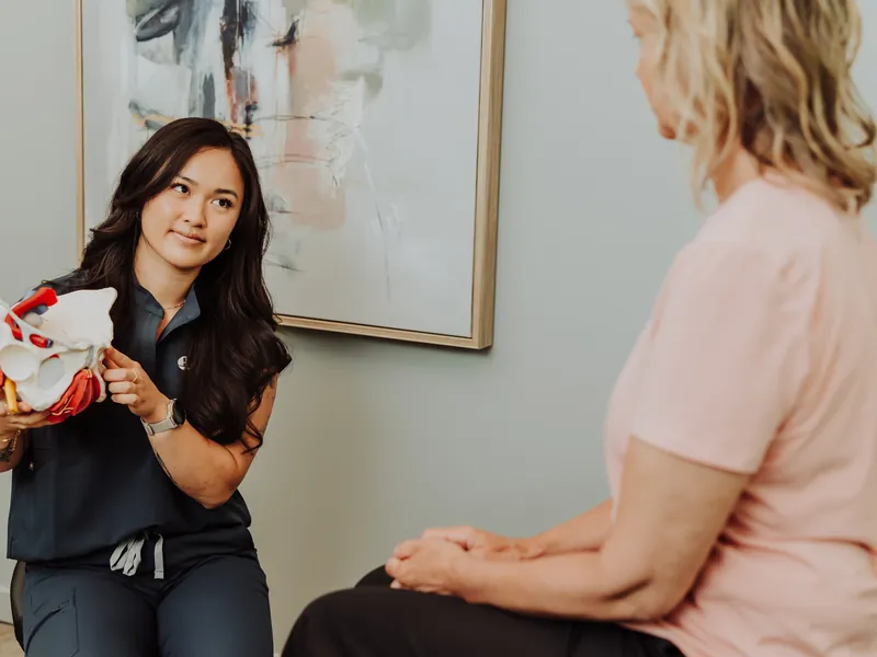 A therapist using a pelvis model to explain the pelvic floor to a patient