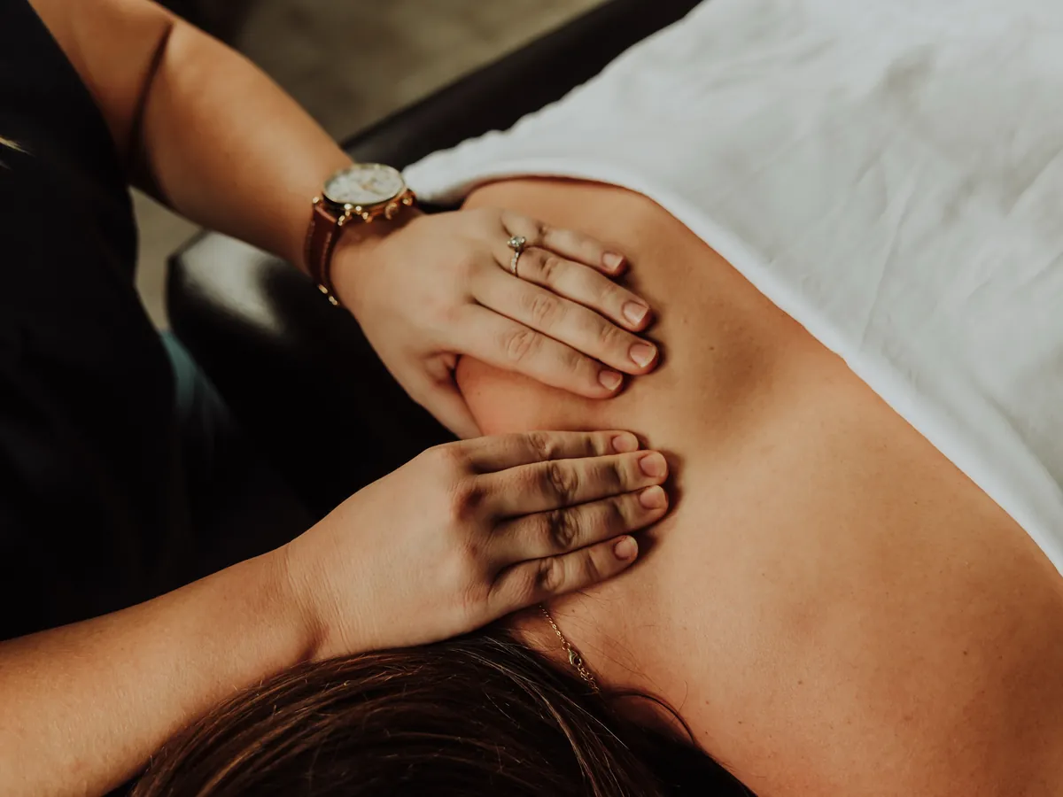 A therapist's hands working on a patient's upper back and shoulder